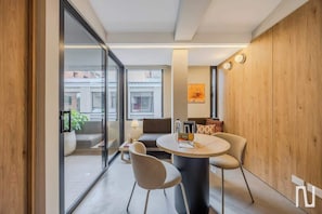 Ein modernes Zimmer mit rundem Tisch, zwei Stühlen, einer Couch und einer Glastrennwand.