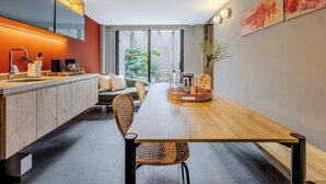 Een moderne keuken met een houten aanrecht, een eethoek met een lange tafel en rieten stoelen, en een groot raam met uitzicht op groen.