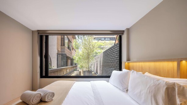 Een hotelkamer met een groot raam, een bed en uitzicht op een smalle steeg.