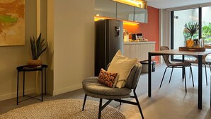 Een moderne woonkamer met een bank, een eettafel en een keuken met een koelkast en kasten.