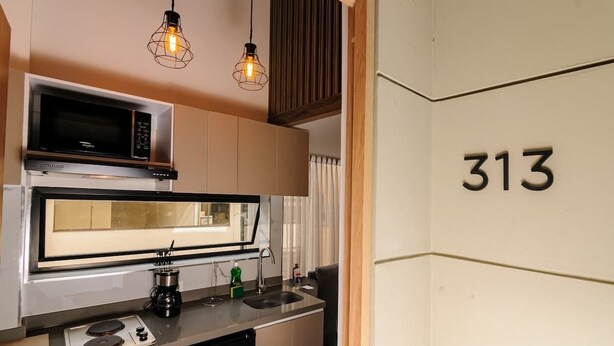 A compact kitchen with a microwave, stove, and sink, and a number '313' on the wall. - NOK Amazing Duplex in Parque 93 (Bogotá)