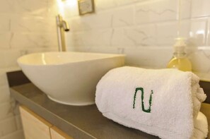 Ein Badezimmer mit einem weißen Waschbecken, einem Handtuch mit einem grünen Buchstaben und einer Seifenspender.