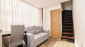 A room with a grey sofa, a wooden door, and a staircase. - NOK Amazing Duplex in Parque 93 (Bogotá)