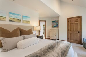 A bedroom with a bed, pillows, a nightstand, a lamp, a dresser, and a door. - Offerson Chalet in Beaver Creek (Beaver Creek)