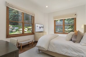 Ein Schlafzimmer mit Bett, Schreibtisch, Stuhl, Fernseher und großen Fenstern mit Blick auf Felsen und Grünflächen.