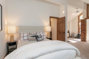 A bedroom with a large bed, two bedside tables with lamps, a wooden door, and a view of a hallway. - Offerson Chalet in Beaver Creek (Beaver Creek)