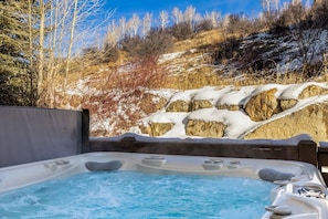 Ein Whirlpool mit Blick auf einen verschneiten Berghang und Bäume.