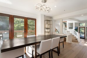 A modern kitchen with a dark wooden island, white chairs, and a glass door leading to a balcony. - Offerson Chalet in Beaver Creek (Beaver Creek)