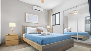 A modern bedroom with a large bed, bedside tables, a mirror, and an air conditioning unit. - NOK Amazing 1BR Apartment Jardines 3, Punta Cana (Punta Cana)