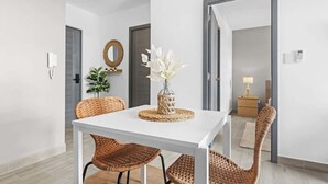 A dining area with a white table and wicker chairs, a vase with white flowers, and a mirror on the wall. - NOK Amazing 1BR Apartment Jardines 3, Punta Cana (Punta Cana)