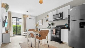 A modern kitchen with white cabinets, stainless steel appliances, and a dining area with wicker chairs. - NOK Amazing 1BR Apartment Jardines 3, Punta Cana (Punta Cana)