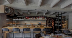 Eine Bar mit Holztresen, Barhocker und einer Auswahl an Flaschen.