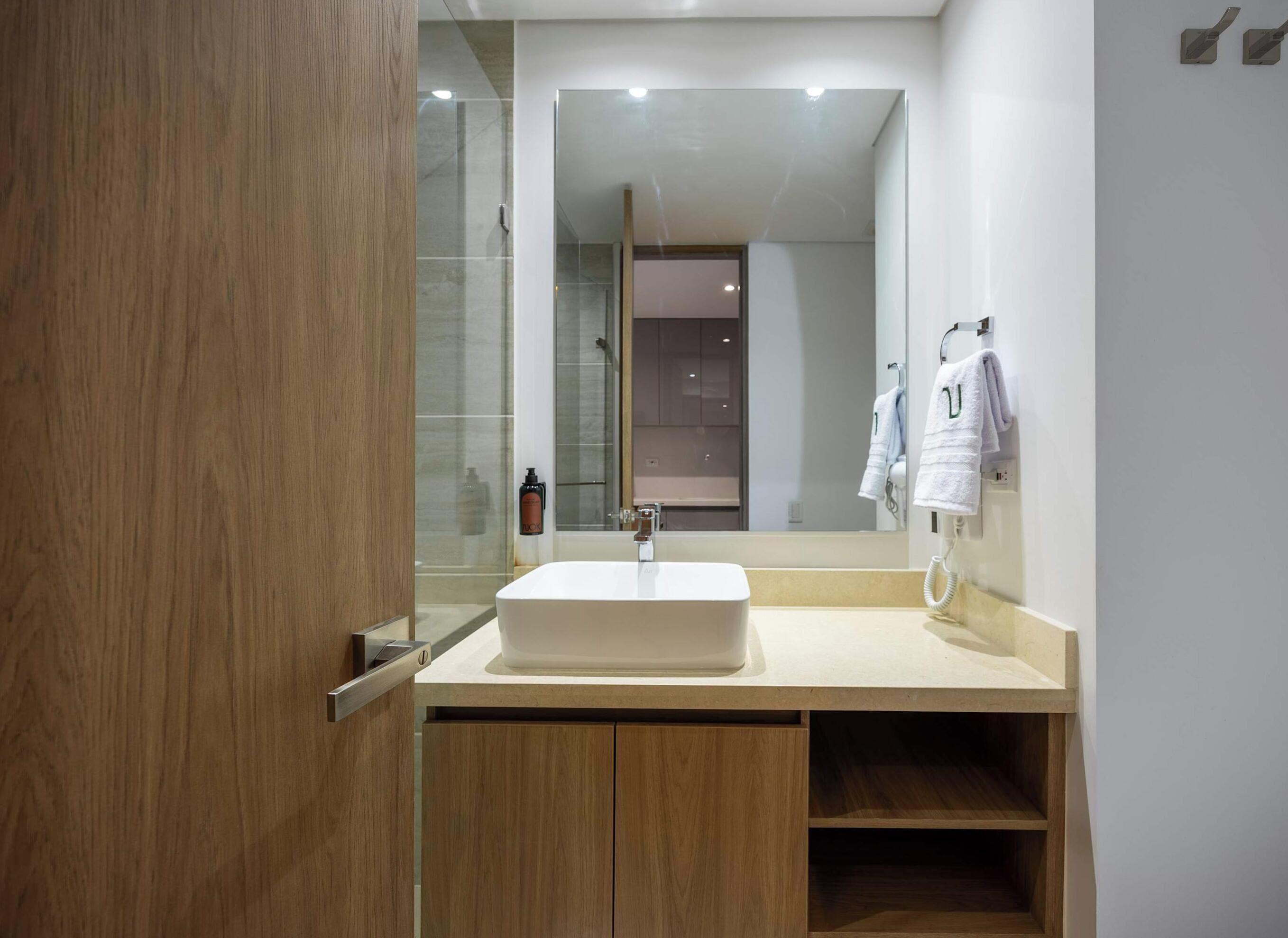 Un baño moderno con un espejo grande, un lavabo rectangular, armarios de madera y una cabina de ducha de cristal.
