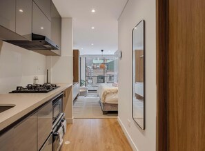 Eine moderne Küche mit Herd, Backofen und Schränken, die in ein Schlafzimmer mit Bett und Blick auf die Stadt führt.