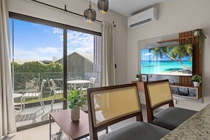 Ein modernes Wohnzimmer mit Fernseher, Sitzgelegenheiten und einem Balkon mit Gartenmöbeln.