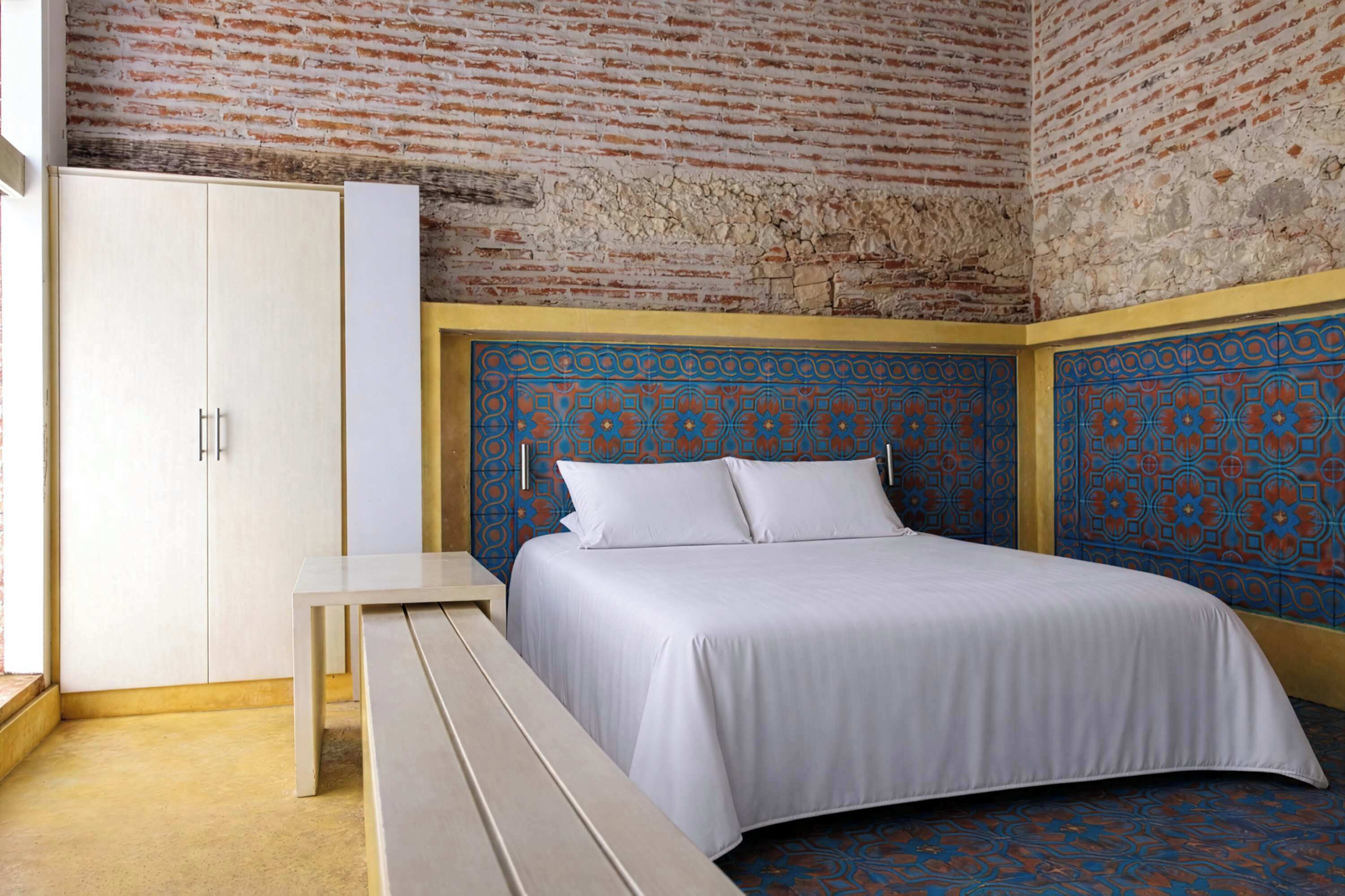 A bedroom with a bed, a bench, a wardrobe, and a patterned wall.