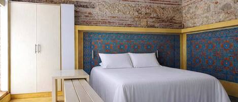 A bedroom with a bed, a bench, a wardrobe, and a patterned wall.