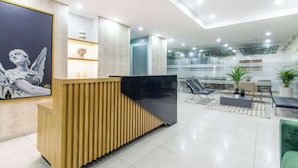 A modern reception area with a wooden reception desk, a large framed artwork, and a seating area with chairs and a sofa. - NOK Designer 2BR in Usaquén (Bogotá)