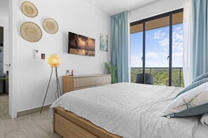 Un dormitorio con cama, mesita de noche, lámpara, una obra de arte en la pared y vistas al exterior.