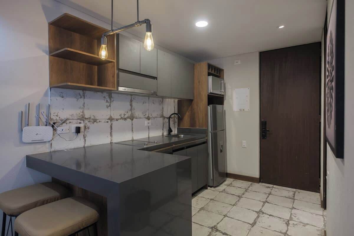 A modern kitchen with a central island, built-in cabinets, a stainless steel refrigerator, and a wooden door.