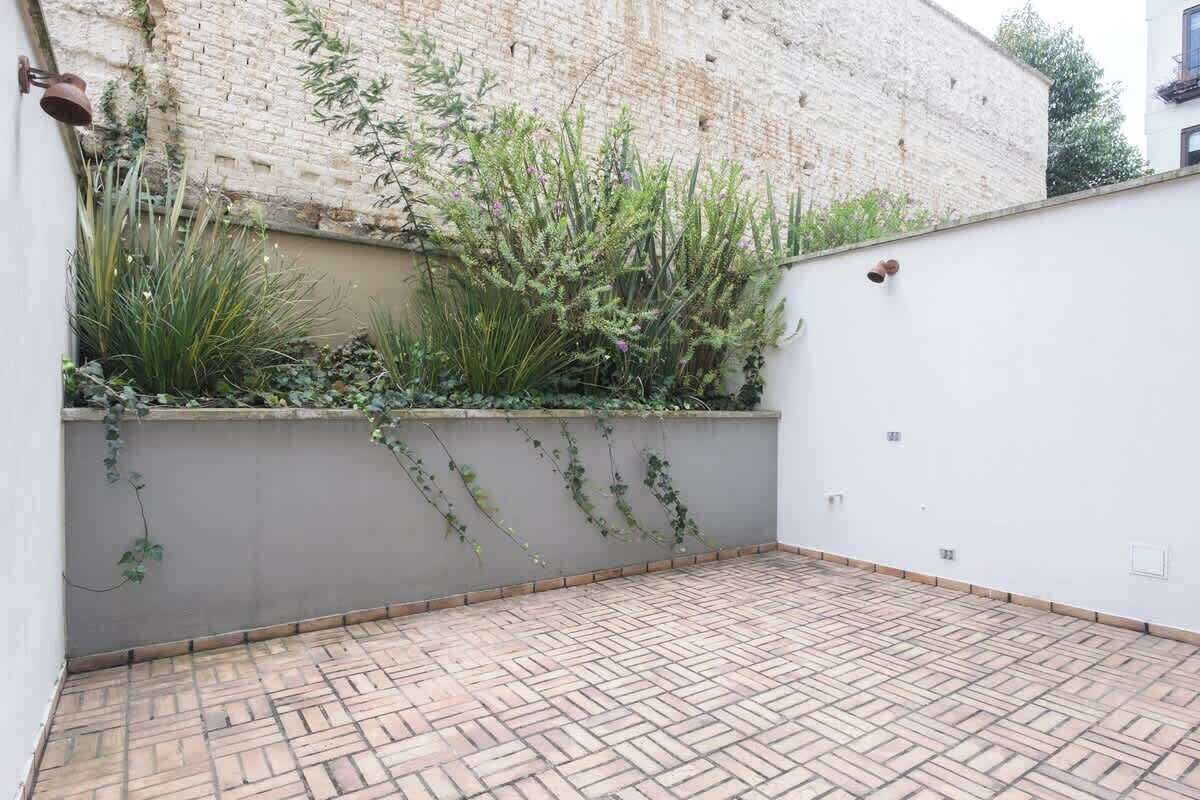 A courtyard with a brick floor, a white wall, and a brick wall with vegetation.