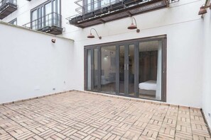 A courtyard with a tiled floor, a sliding glass door leading to a room, and a balcony with metal railings. - NOK Amazing 1 Br in Candelaria (Bogotá)