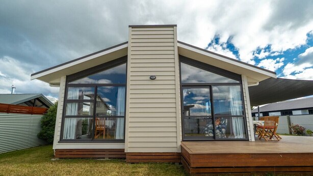 Ett modernt hus med ett stort glasfönster, en träveranda och ett staket av metall.