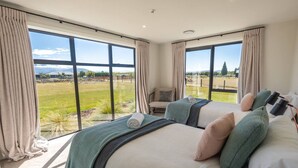 Ein Schlafzimmer mit zwei Betten, großen Fenstern, einem Sessel und Blick auf ein grünes Feld.
