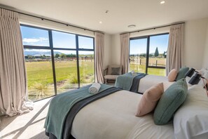 A bedroom with two beds, large windows, a chair, and a view of a grassy field. - Ben Ohau Vista Lodge | Stunning Mountain Views (Twizel)