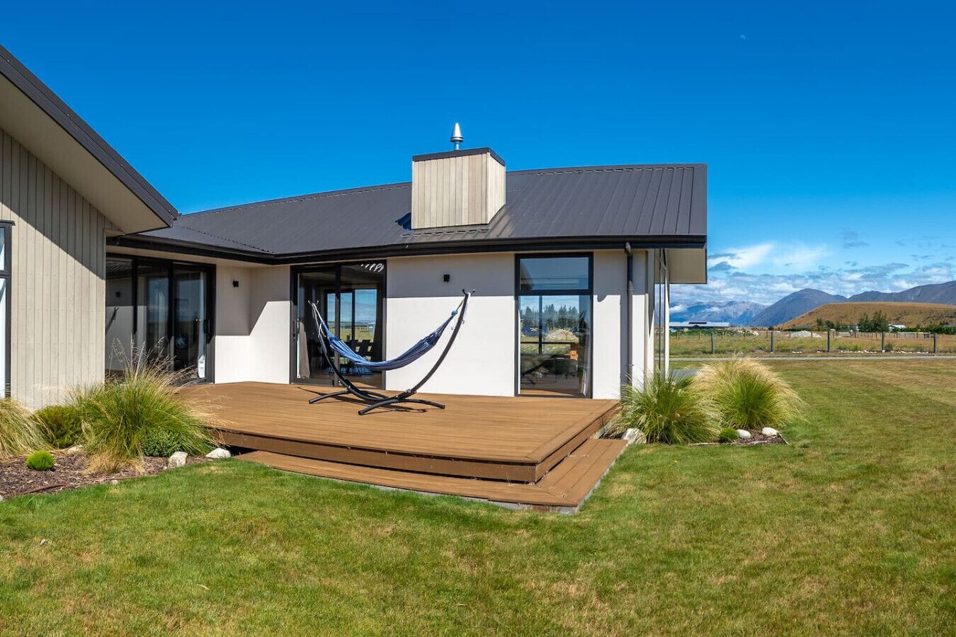 A modern house with a wooden deck, a hammock, and a view of mountains.