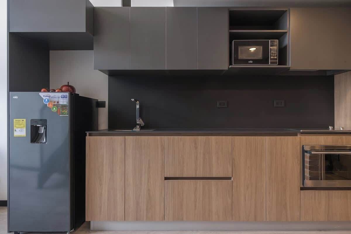 A modern kitchen with a built-in microwave, a stainless steel refrigerator, and wooden cabinets.