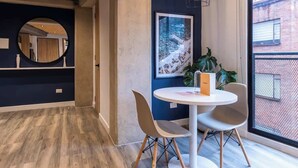Un intérieur moderne avec une table ronde, deux chaises, un tableau encadré et une grande fenêtre.