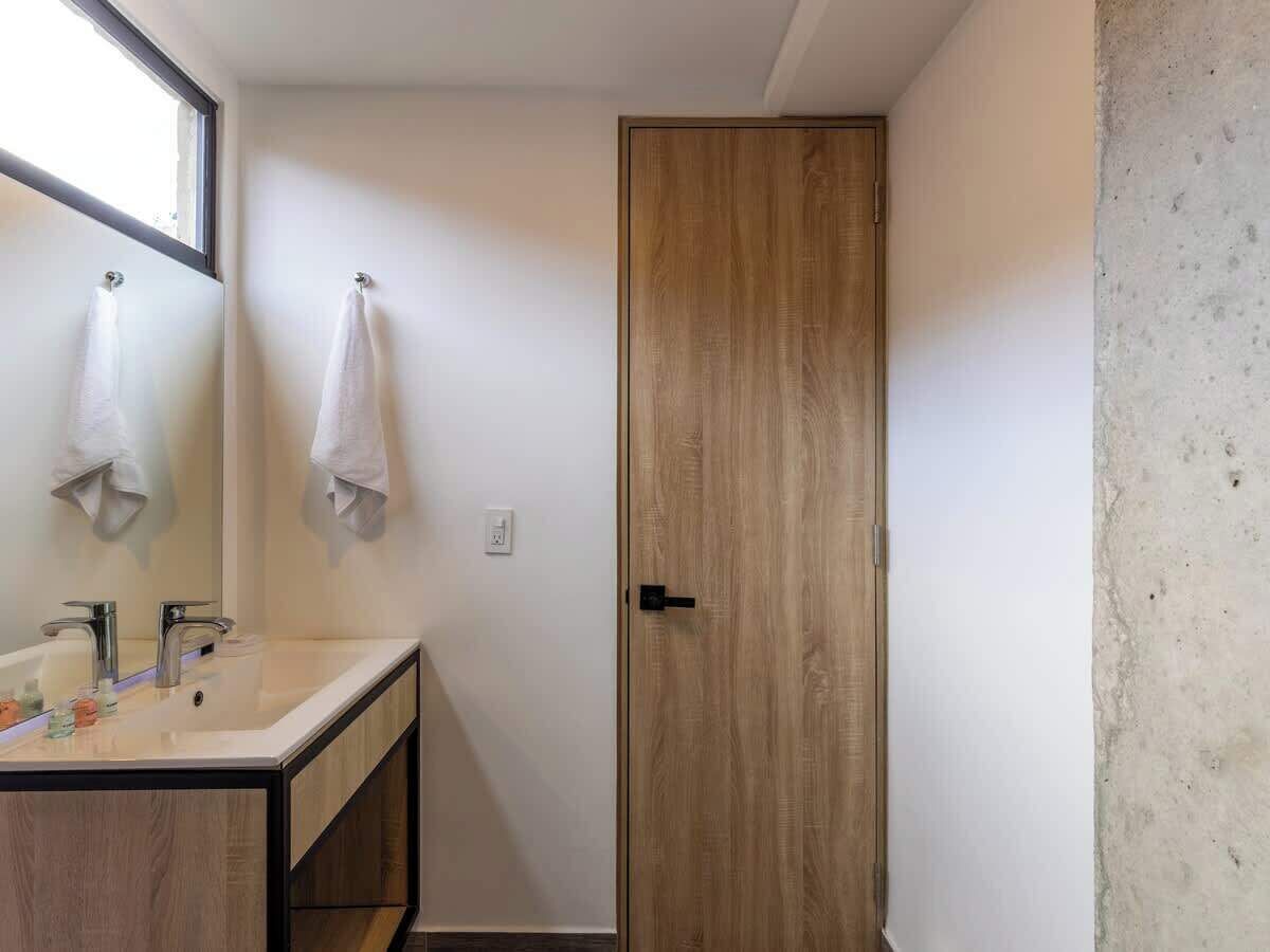 Ein Badezimmer mit Holztür, Waschbecken mit Spiegel und zwei Handtüchern, die an Haken hängen.