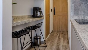 Een smalle keuken met een koffieapparaat op een plank, een houten deur en een prullenbak.