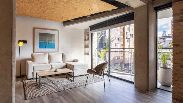 A modern living room with a sofa, armchair, coffee table, and a painting on the wall. - NOK Stunning 1 BR in Chapinero (Bogotá)
