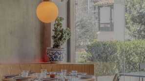Un coin repas avec une table dressée pour deux personnes, une plante en pot et une grande fenêtre donnant sur un paysage verdoyant.