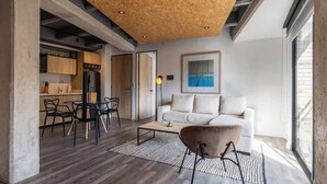 A modern living room with a wooden ceiling, a white sofa, a coffee table, and a dining area with chairs and a kitchen in the background. - NOK Stunning 1 BR in Chapinero (Bogotá)