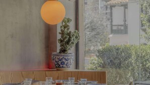 Et spiseområde med et bord dækket til fire personer, en potteplante og en hængende lampe.