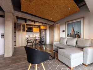 Ein modernes Wohnzimmer mit grauem Sofa, schwarzem Sessel, Couchtisch aus Holz und einem Stadtbild an der Wand.
