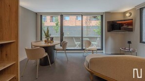 Ein modernes Zimmer mit einem runden Esstisch, zwei Stühlen, einer Couch und einem großen Fenster mit Blick auf Gebäude.