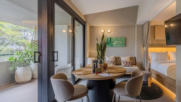 Een moderne hotelkamer met een ronde eettafel, twee stoelen, een bank, een bed en een groot raam.