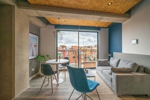 Ein modernes Wohnzimmer mit einer Couch, einem Esstisch mit Stühlen und einem großen Fenster mit Blick auf die Stadt.