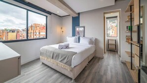 A modern hotel room with a large window, a bed, a desk, and a bookshelf. - NOK Bright Loft in Chapinero (Bogotá)