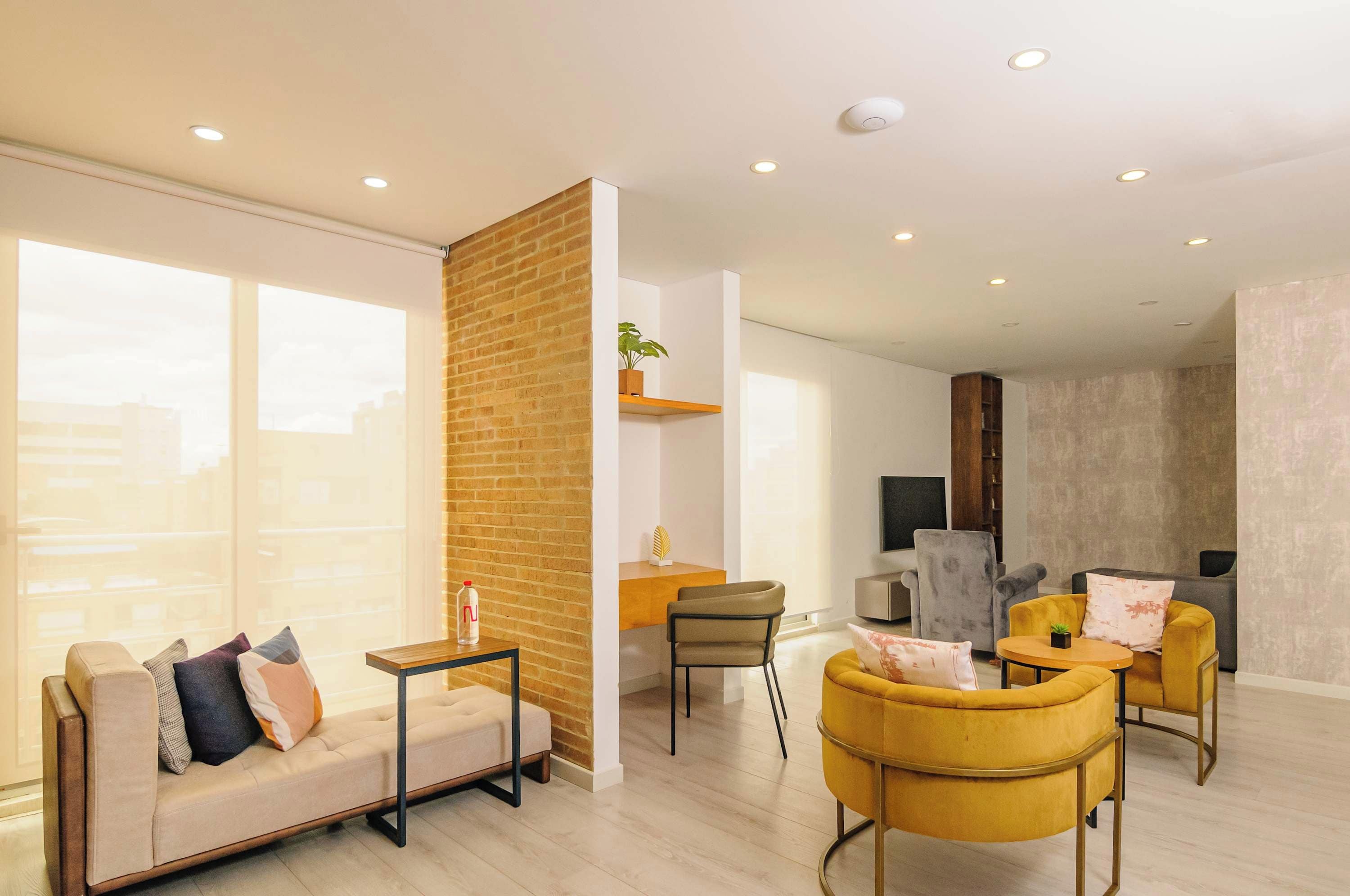 A modern living room with a sofa, chairs, a coffee table, a TV, and a brick accent wall.