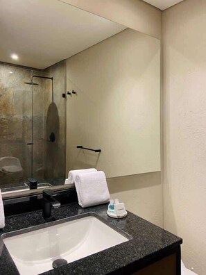 A modern bathroom with a large mirror, a granite countertop, a sink, and a glass-enclosed shower. - NOK Great Studio (Bogotá)