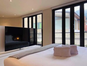 A modern hotel room with a large bed, a flat-screen TV, and large windows offering a view of the outdoors. - NOK Great Studio (Bogotá)