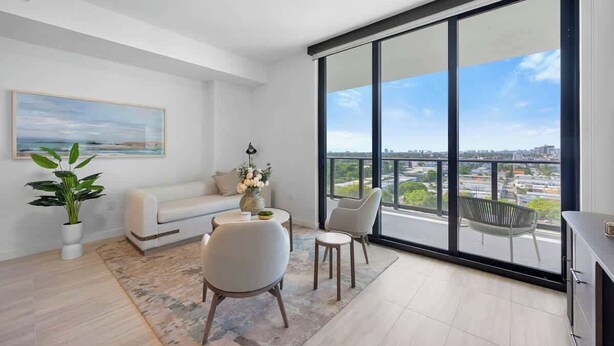 A modern living room with a sofa, two chairs, a coffee table, a large window with a city view, and a painting on the wall. - NOK Luxury 2BR in Miami Beach (Miami Beach)