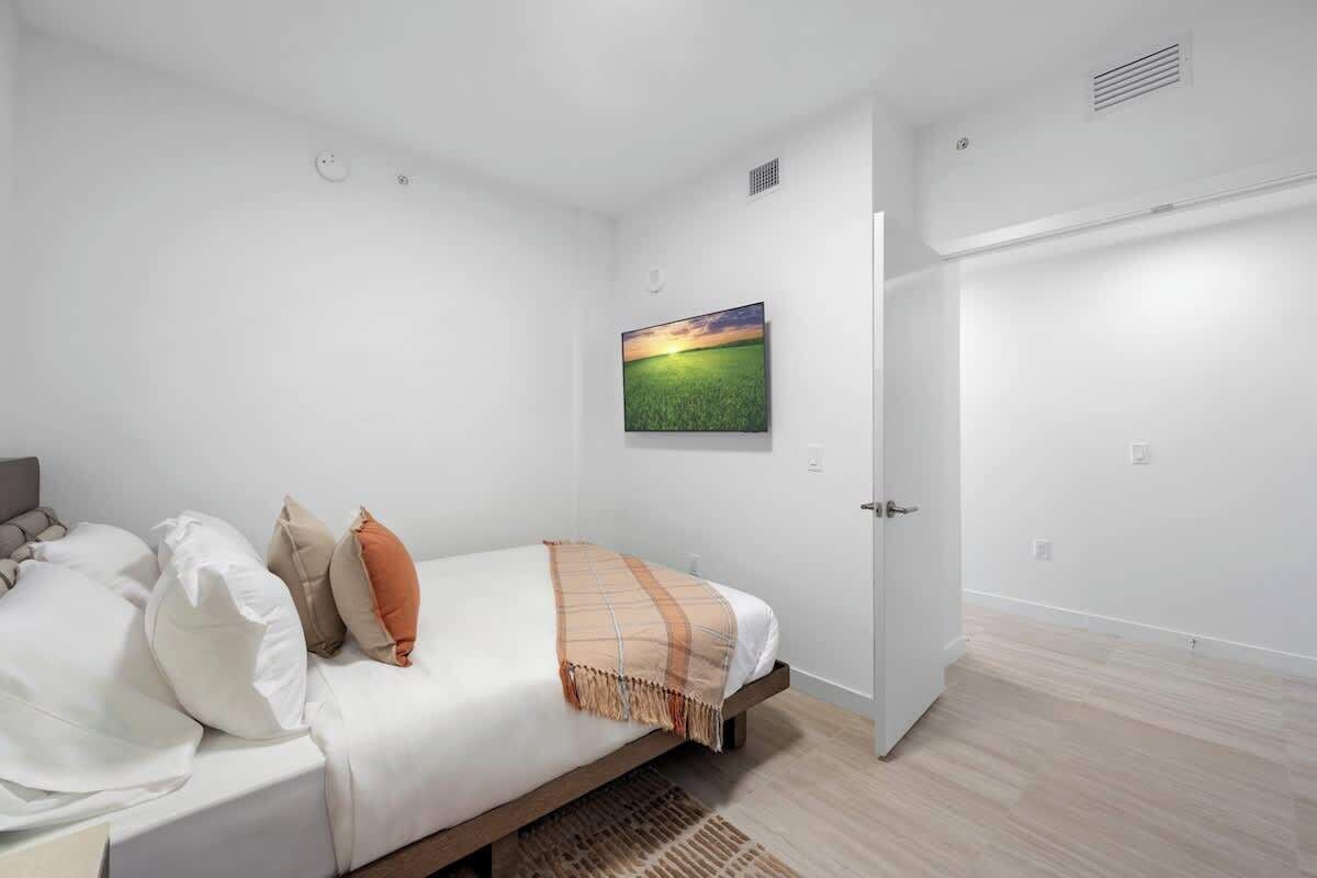 A bedroom with a bed, pillows, a blanket, a painting, and a door.