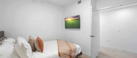A bedroom with a bed, pillows, a blanket, a painting, and a door.