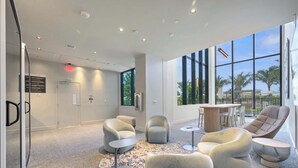 A modern lounge area with seating, a small table, and large windows offering a view of palm trees. - NOK Luxury 2BR in Miami Beach (Miami Beach)
